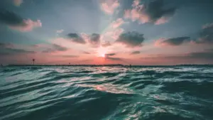 Sanfter Sonnenuntergang über bewegter Wasseroberfläche in stimmungsvollen Lila- und Blautönen.